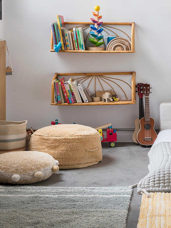 A cozy children's corner with plush seating, shelves filled with books and toys, a guitar, and colorful rugs.