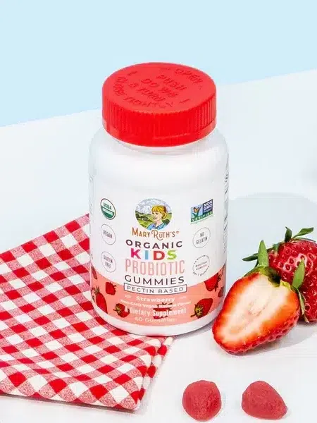 A bottle of maryruth's organic kids probiotic gummies with strawberries and gummy supplements on a white surface beside a red and white checkered napkin.