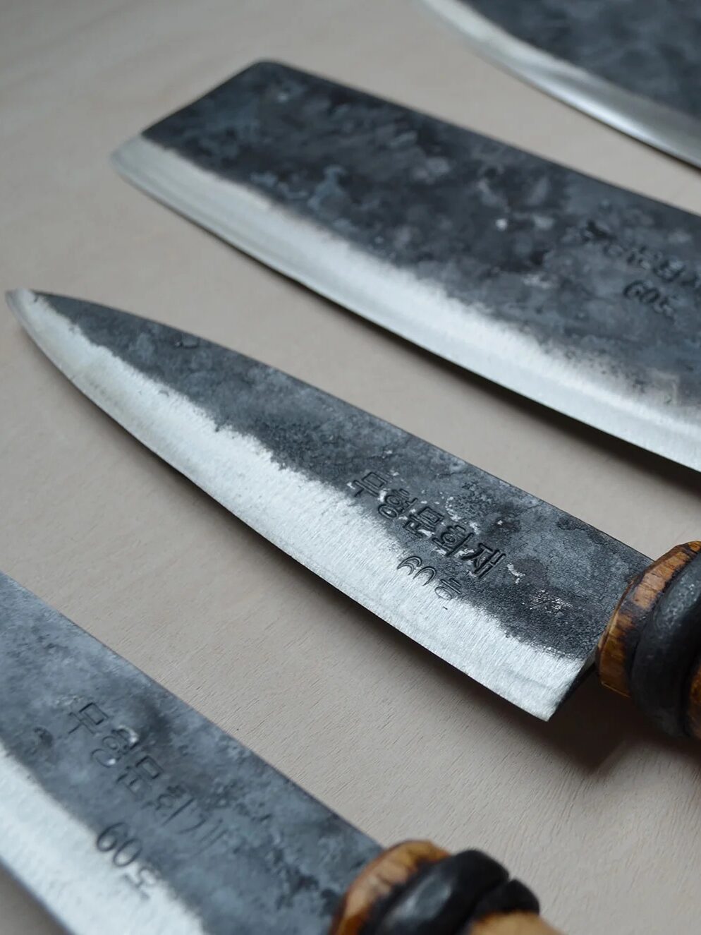 Three rustic kitchen knives with wooden handles and inscribed blades, displayed on a wooden surface.