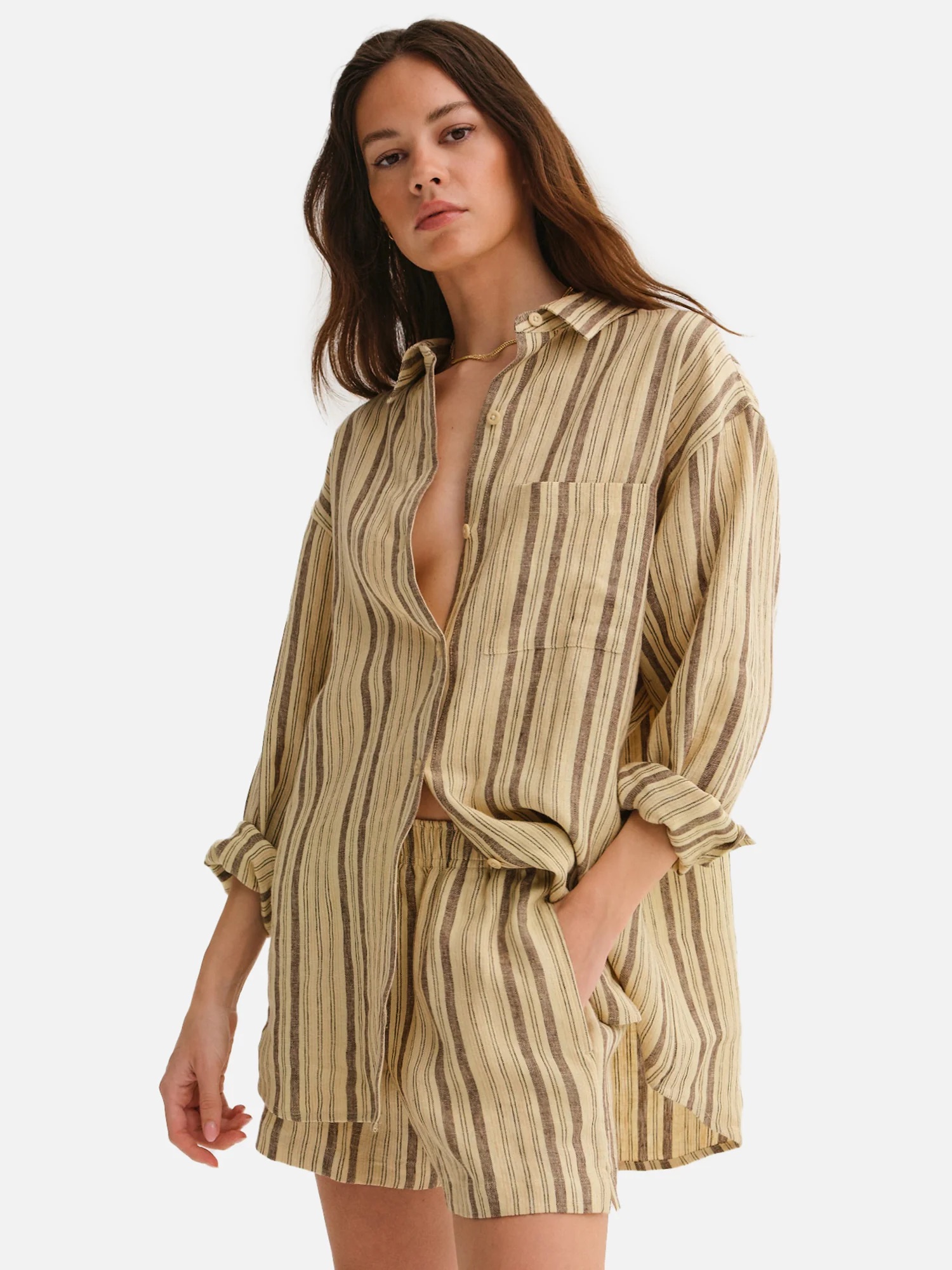 A woman wearing a loose-fitting striped shirt-dress, standing with one hand slightly raised, against a plain background.