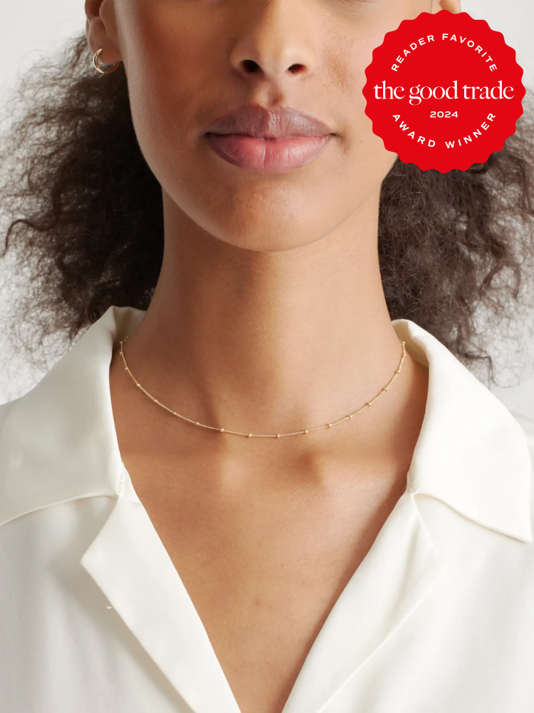 Close-up of a woman wearing a delicate gold necklace and a white blouse, with a text overlay stating "reader favorite 2024, the good trade award winner.