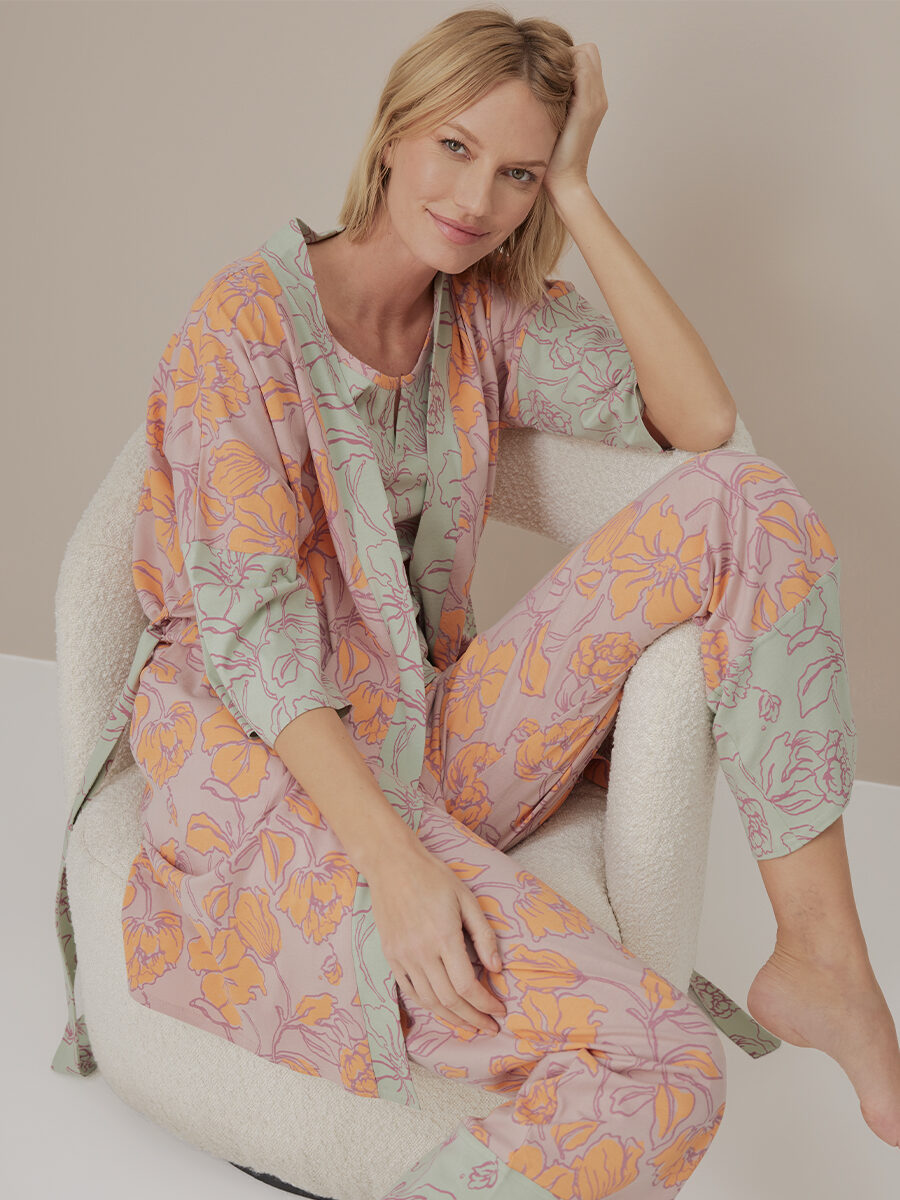 Woman in floral pajamas sitting relaxed in a textured armchair, gracefully posing with one hand on her head.