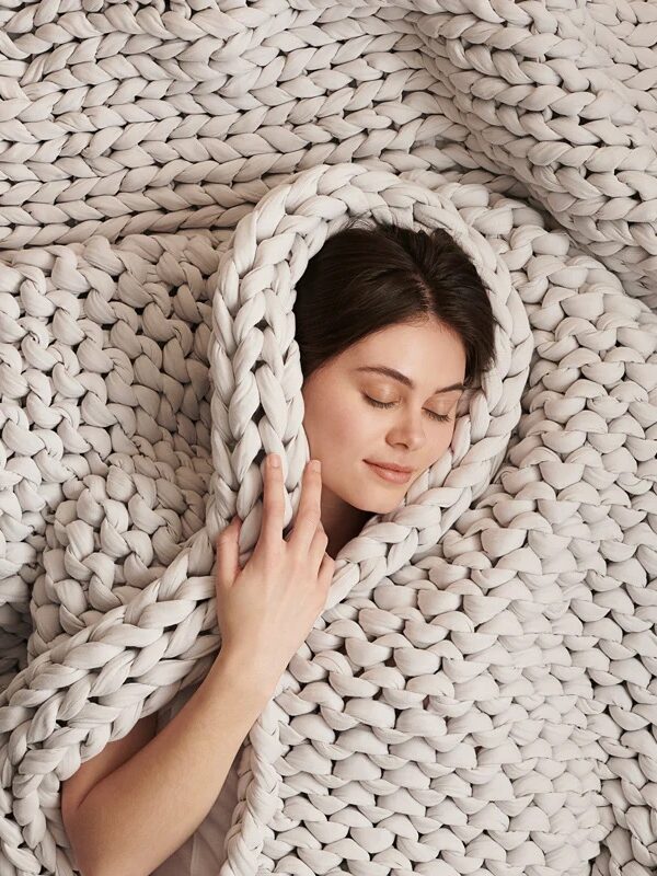 Woman resting peacefully with her head wrapped in a thick, knitted beige blanket, creating a cozy and serene atmosphere.