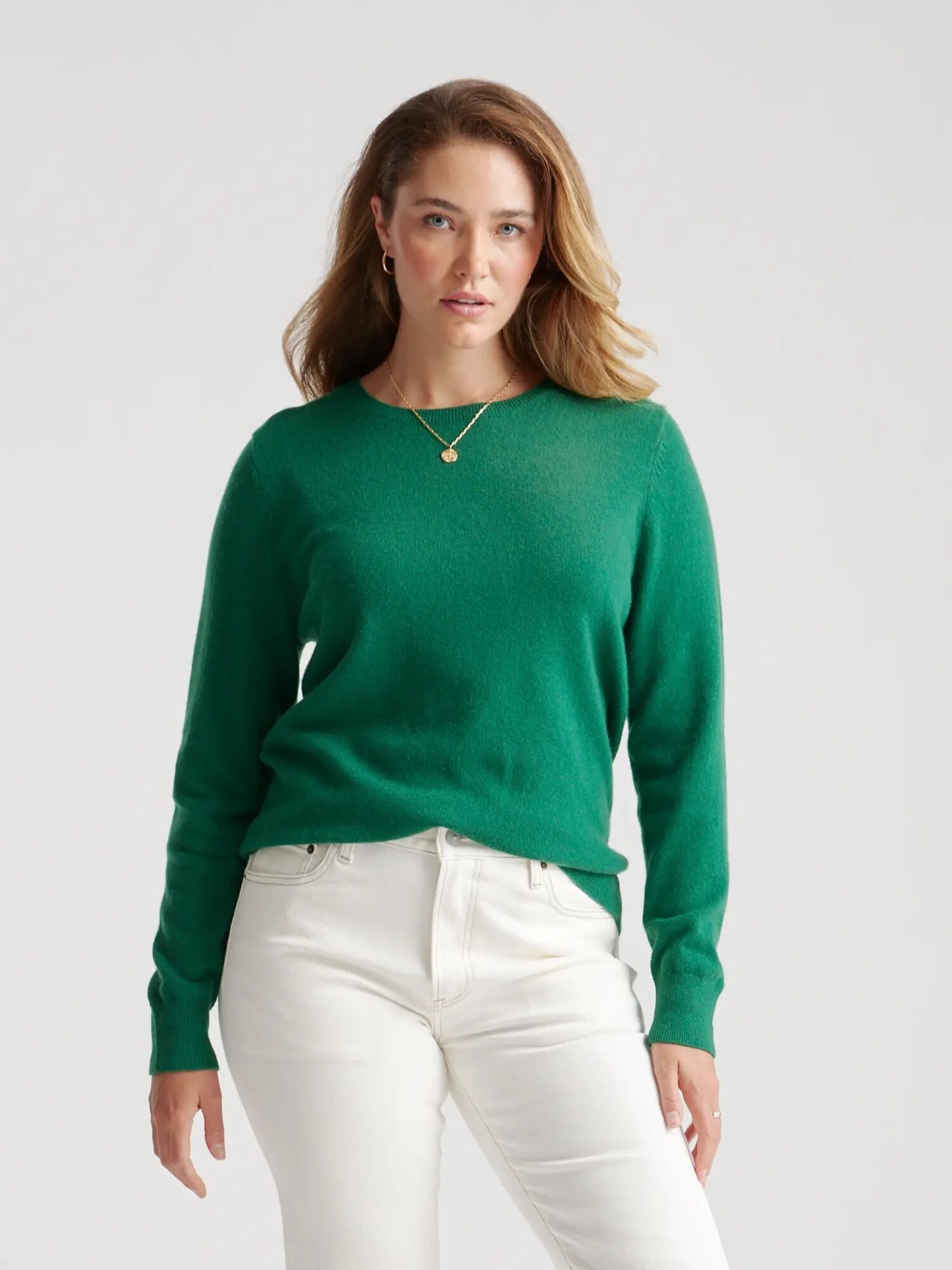 A woman in a green sweater and white pants against a plain background, looking directly at the camera.