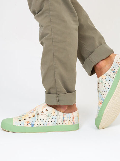 Person wearing patterned sneakers and rolled-up olive trousers against a white background.