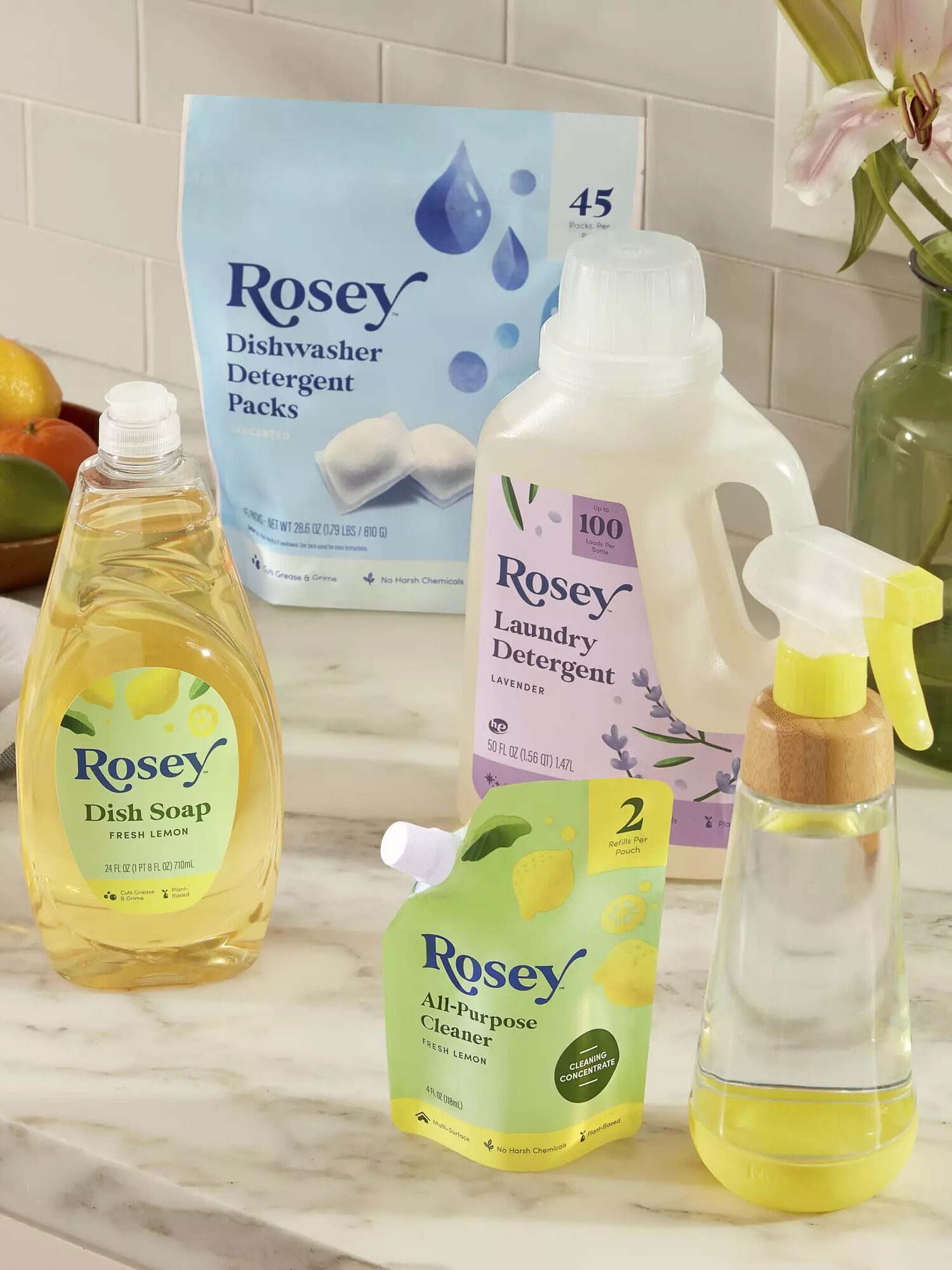 A collection of household cleaning products on a kitchen counter, including dish soap, dishwasher detergent packs, laundry detergent, and all-purpose cleaner.