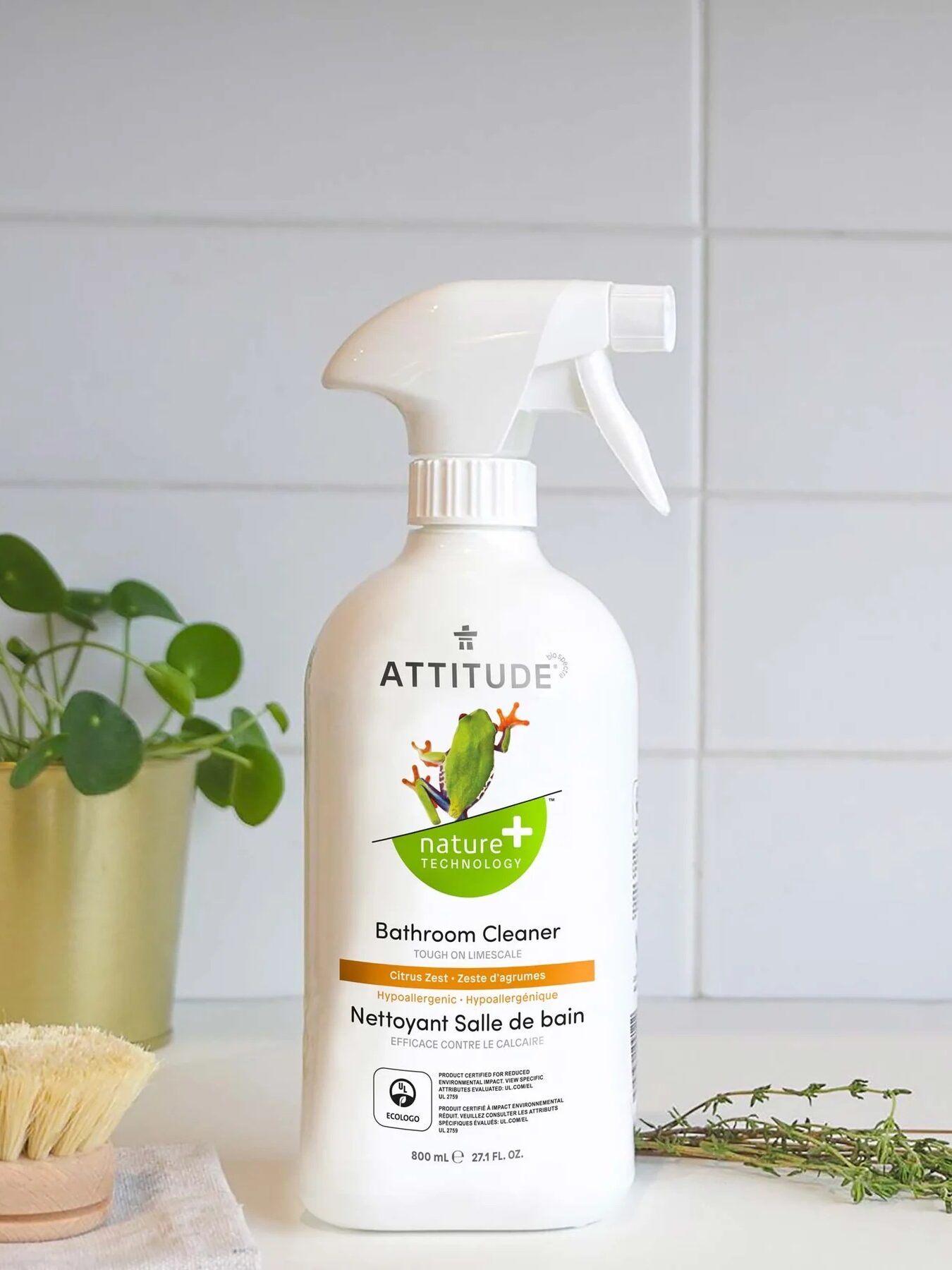 Bathroom cleaner spray bottle on a kitchen countertop with natural scrub brush and plants.