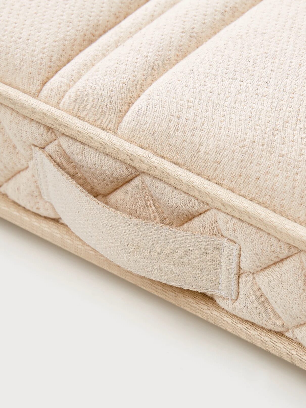 Close-up of a beige fabric mattress corner with a handle.