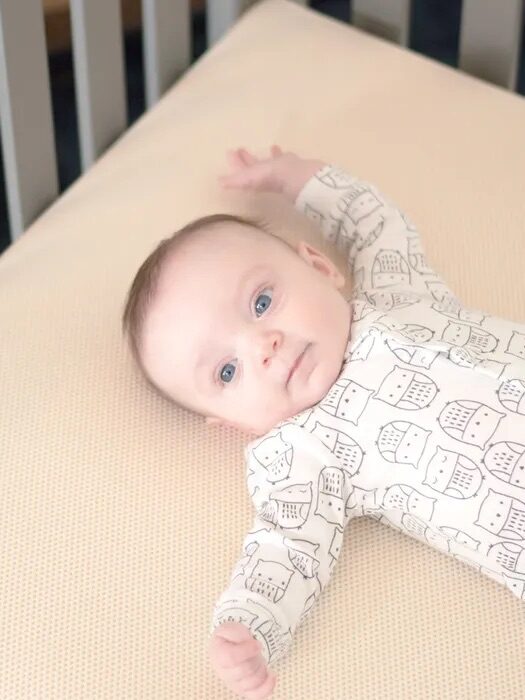 An infant lying on its back on a changing pad with one arm raised.