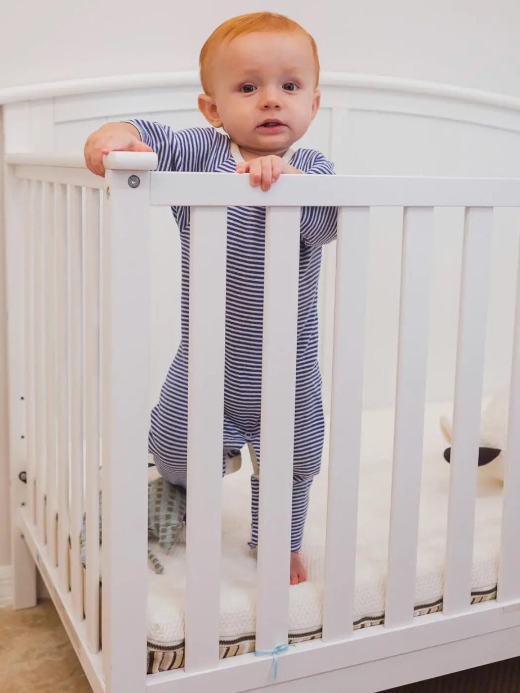 Toddler standing up in a crib, holding onto the rail.