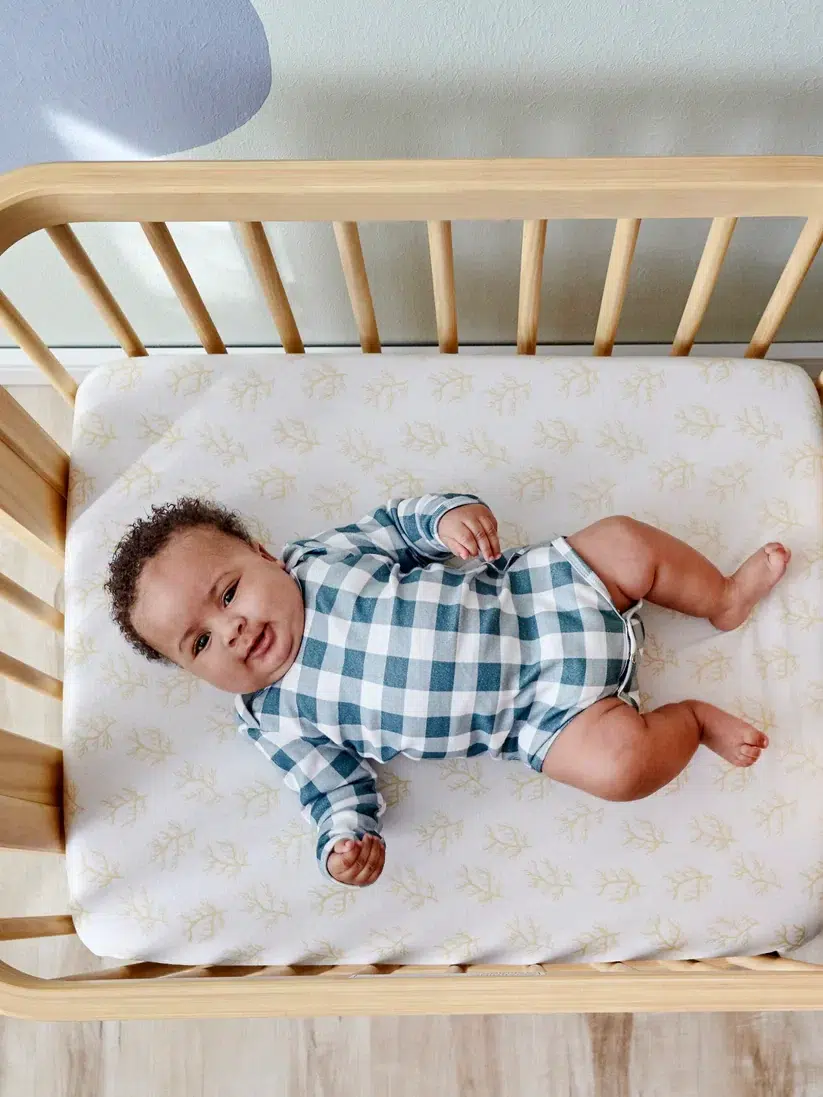 Infant lying peacefully in a wooden crib with a patterned mattress.