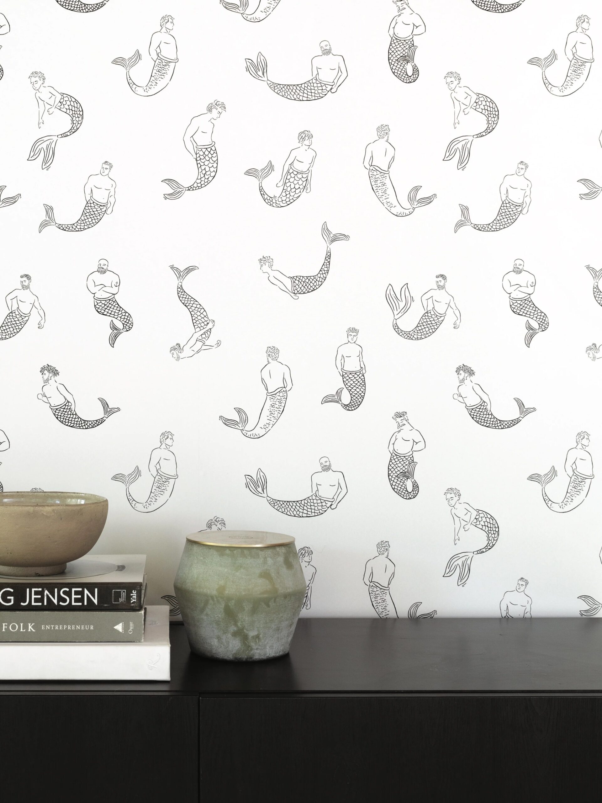 Wallpaper featuring a repeating pattern of mermaids, with a shelf holding a bowl, books, and a decorative stone object.