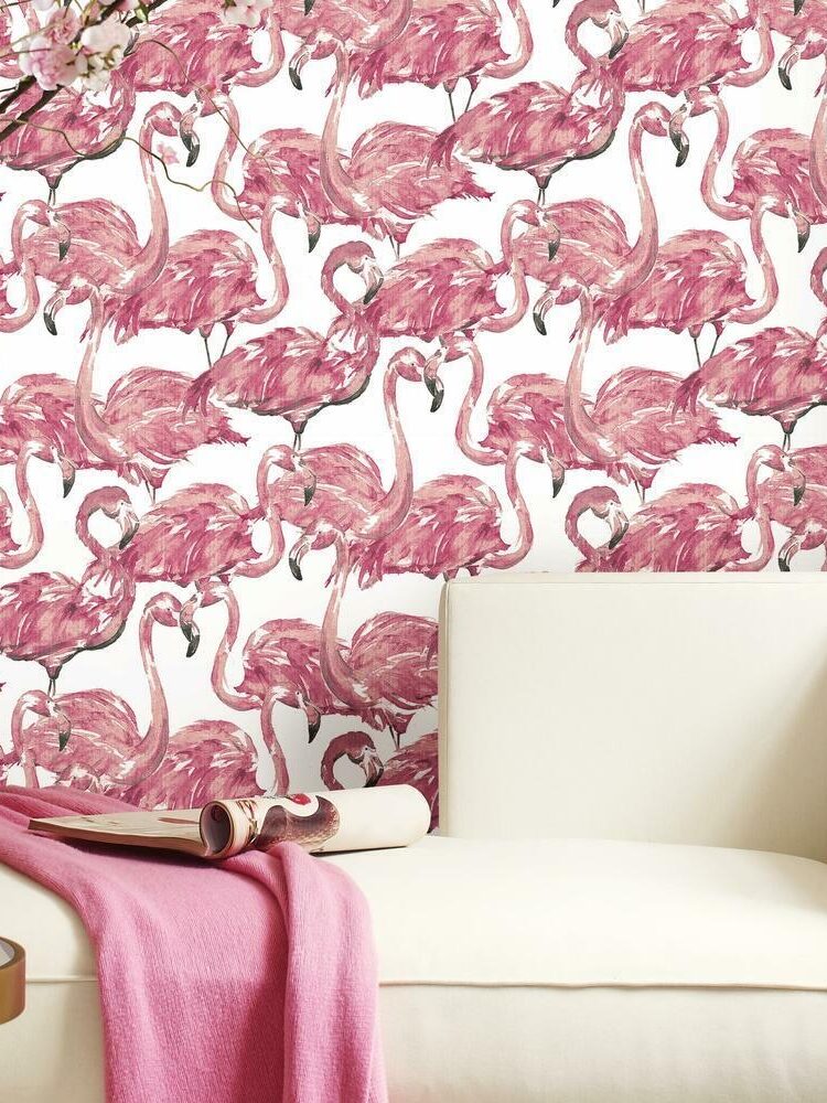 A modern room corner with white sofa and a pink throw, against a wall covered in vibrant pink flamingo wallpaper.