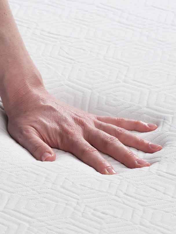 A hand resting on a textured white mattress, emphasizing the softness and contours of the fabric.