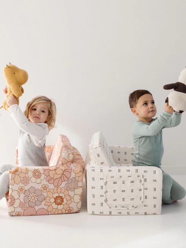 Two children playing with stuffed animals and cardboard blocks shaped like smaller pieces of furniture.