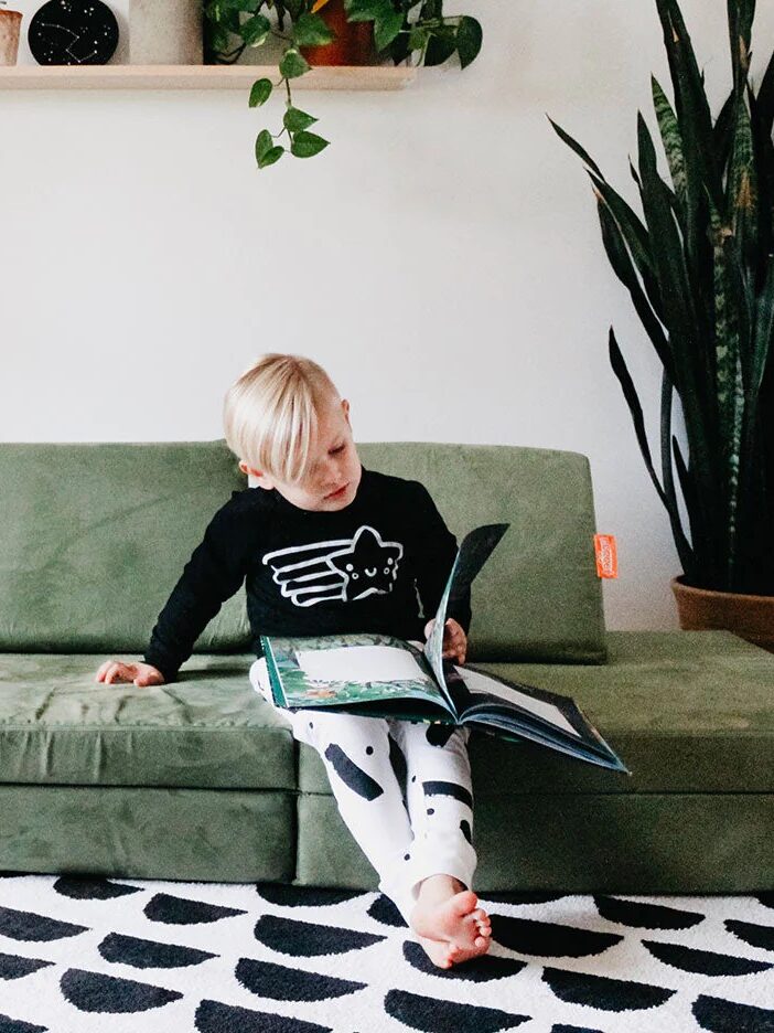 A child reading a book on a green couch in a modern living room.