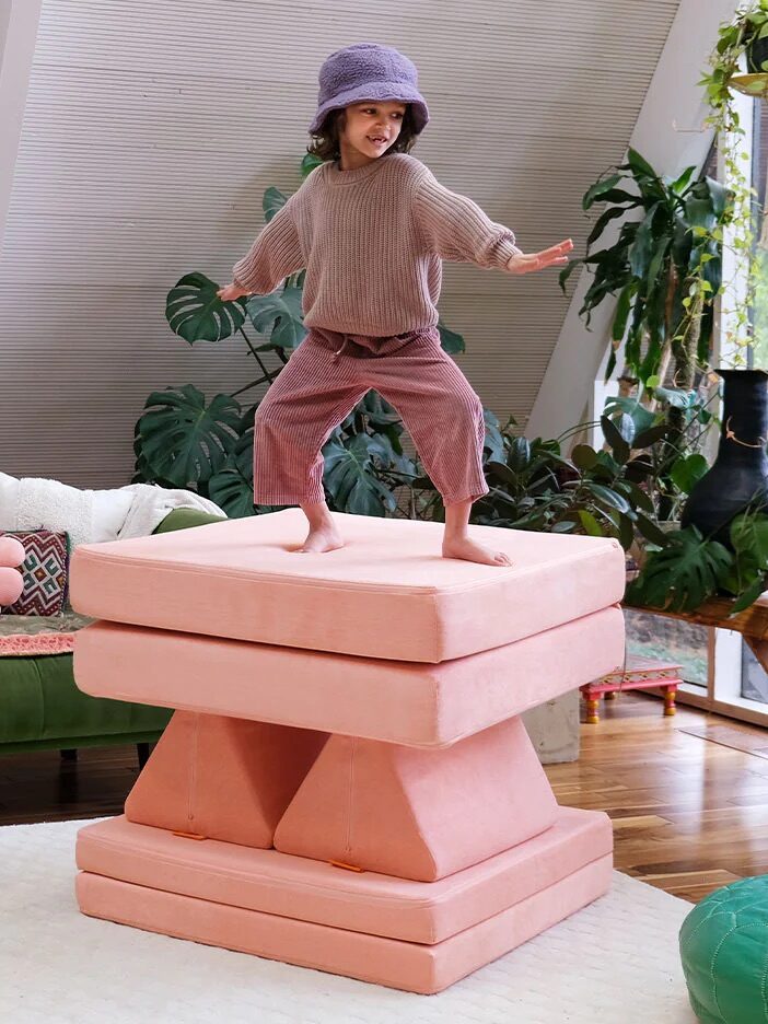A child balancing on stacked cushioned play shapes in a bright indoor playroom.