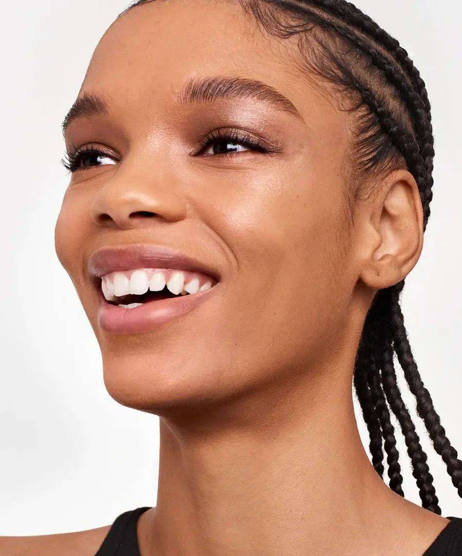 Close-up of a smiling woman with braided hair, looking upward to her left. she has clear skin and is wearing minimal makeup.
