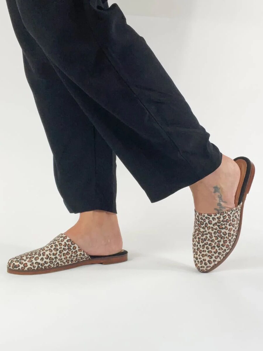 Person wearing leopard print loafers and black trousers against a white background.