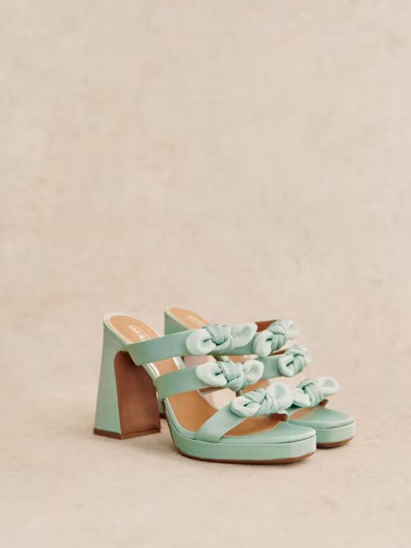A pair of mint green high-heeled sandals with floral embellishments on a beige background.