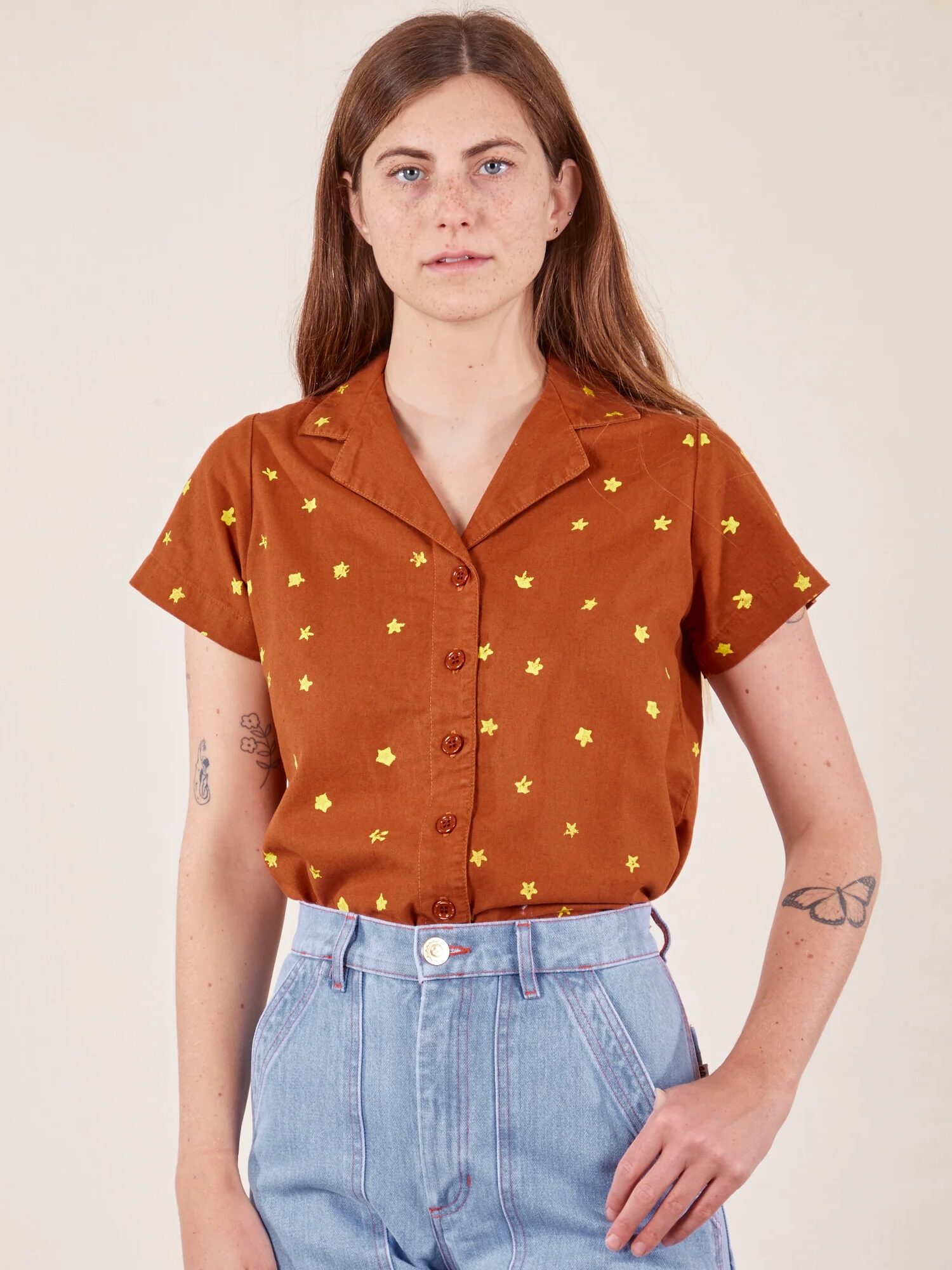 Woman posing in a rust-colored star-patterned shirt and light blue jeans.