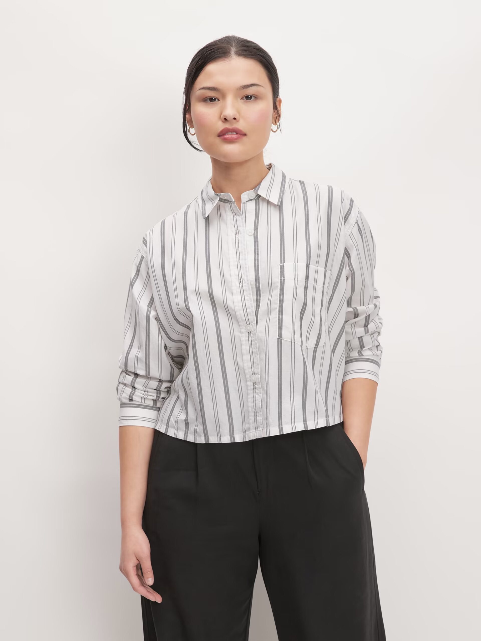 Woman posing in a striped shirt and black trousers against a white background.