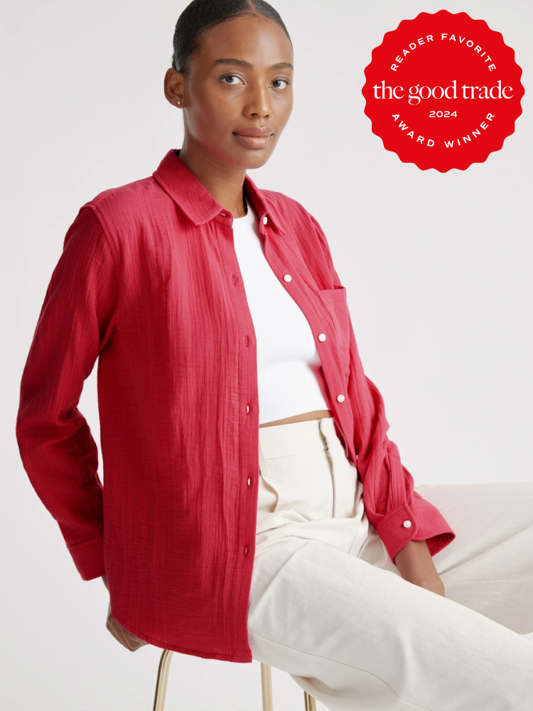 A model seated on a stool wearing an open button down shirt in red, with a white crop top and white pants. 