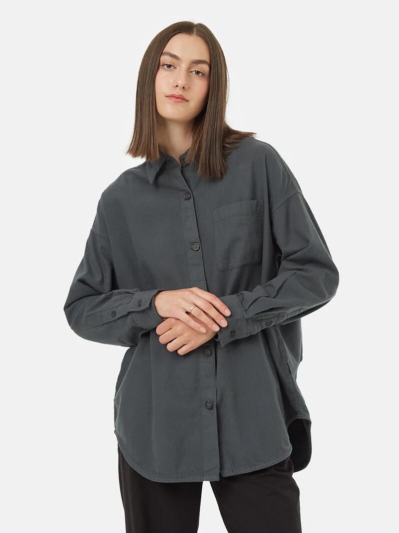 A woman wearing a gray oversized button-up shirt with her hands lightly clasped in front of her.