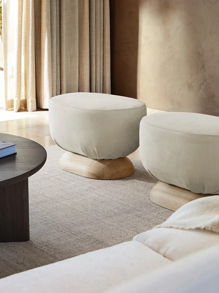 Two white ottomans with wooden bases next to each other in a room. 