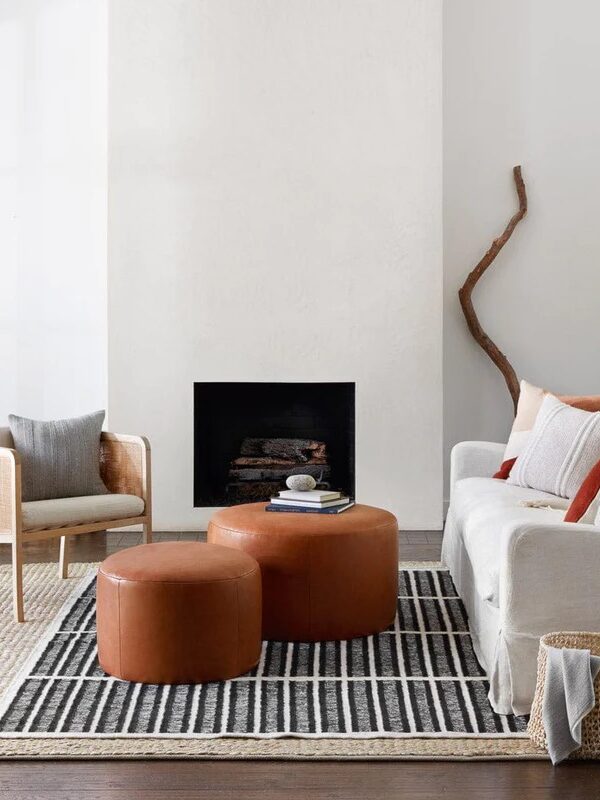 A minimalist living room with two chairs, a sofa, two round leather ottomans, a fireplace, and neutral decor.