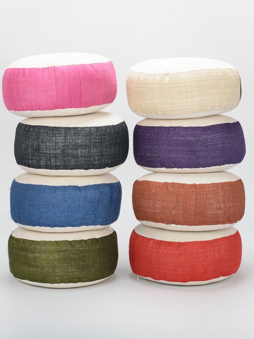 A stack of colorful round meditation cushions in various colors including pink, white, black, blue, green, and red.