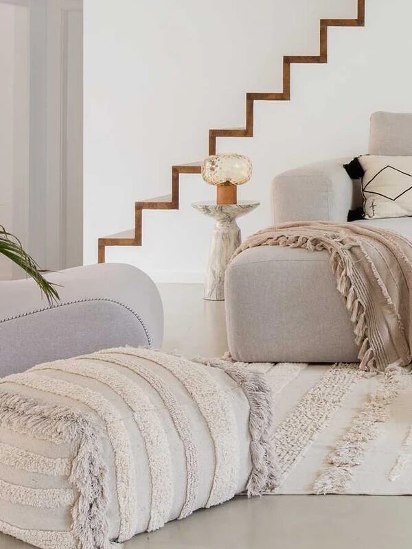 A cozy living room with a plush sofa, decorative throw pillows, a fringed blanket, and a stylish floating staircase.