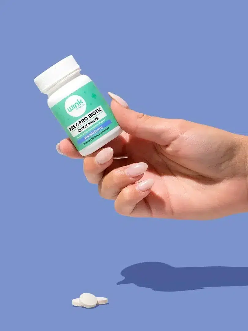 A hand holding a bottle of dietary supplements against a blue background.