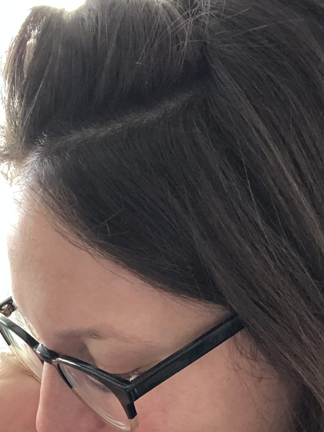 Close-up of a woman with glasses smiling down at a baby, partial view of baby's face visible.