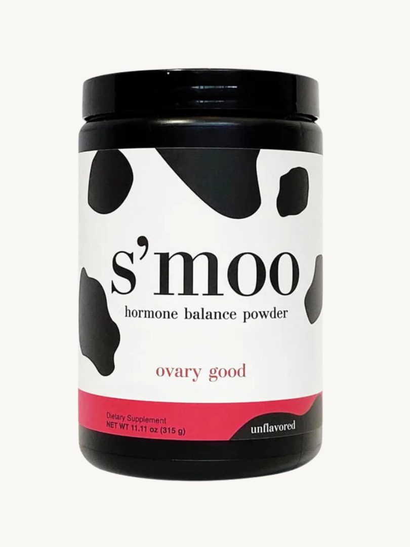 A jar of s'moo hormone balance powder labeled "ovary good," unflavored, against a white background. the jar features black and white cow spots with pink accents.
