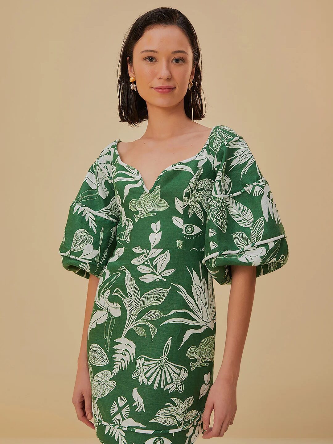 A woman wearing a green and white tropical print dress, standing confidently against a beige background.