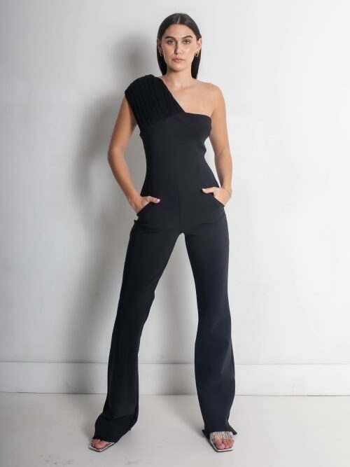 A woman in a stylish black one-shoulder jumpsuit poses against a white background.