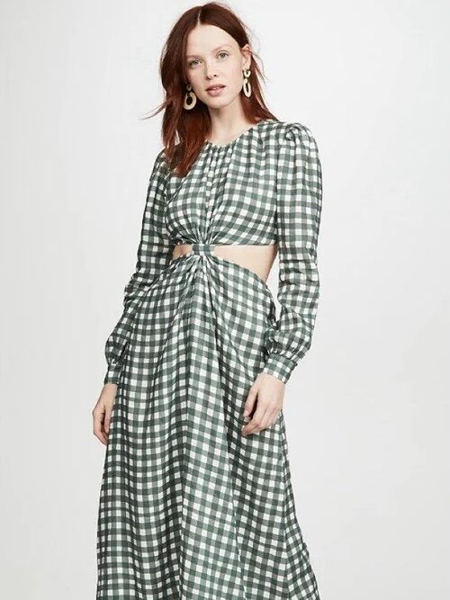 A woman modeling a green and white gingham outfit comprising of a cropped blouse and flowing skirt, standing against a plain backdrop.