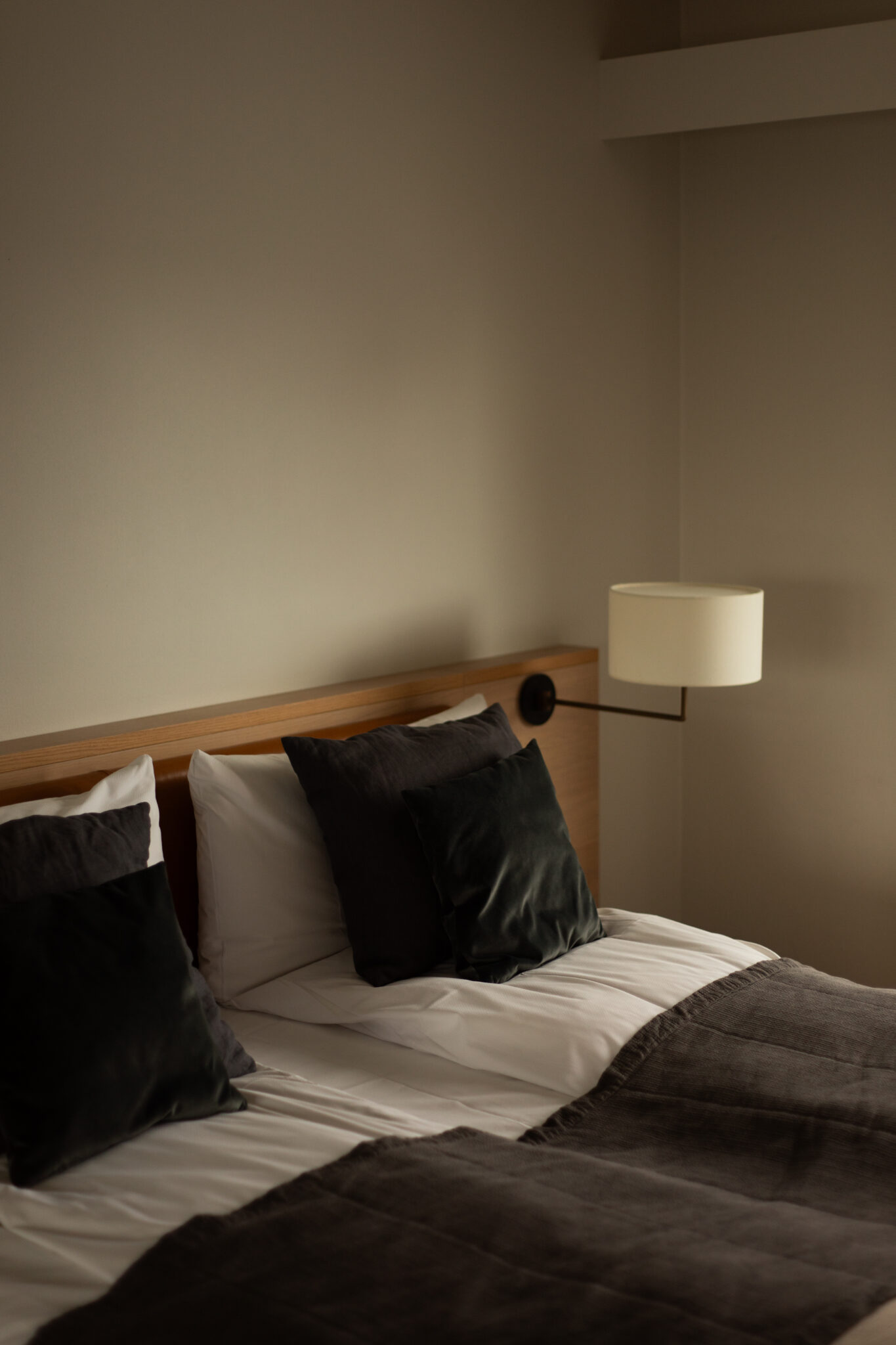 A modern bedroom featuring an unmade bed with white and grey bedding, flanked by a wall-mounted lamp.