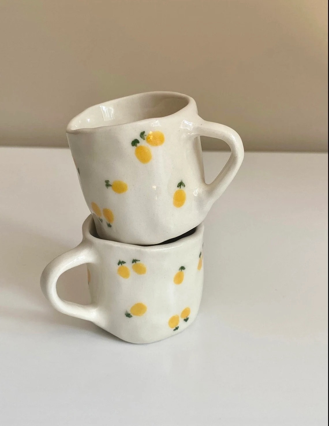 Two white ceramic cups with yellow fruit patterns stacked on a table against a plain background.