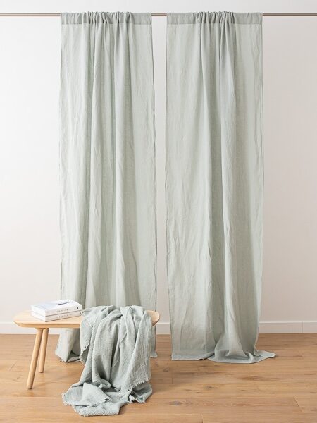 Light green curtains hanging on a rod near a wall, with a small wooden table and a draped matching cloth.