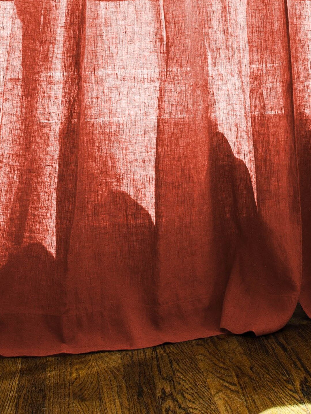 Sunlight casting shadows on a wooden floor through a translucent red curtain.