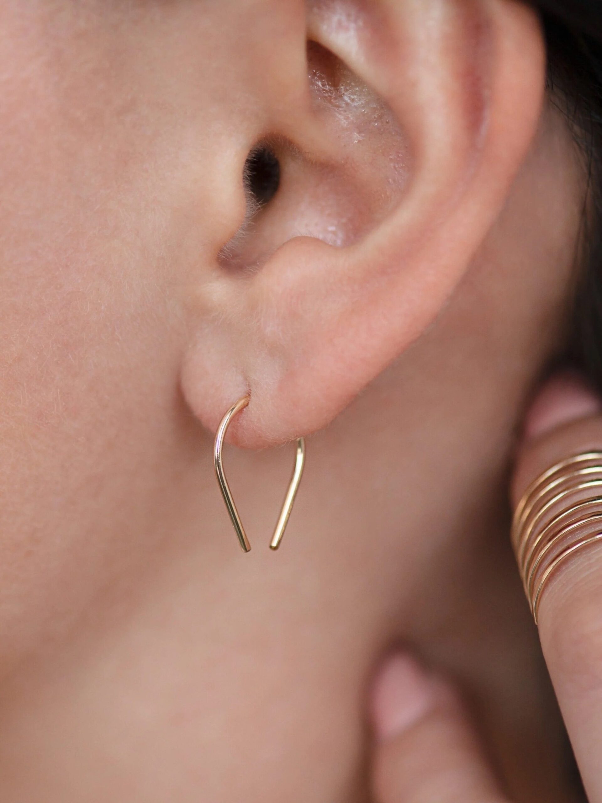 Close-up of a woman's ear wearing a simple gold hoop earring, with a focus on elegant jewelry and subtle makeup.