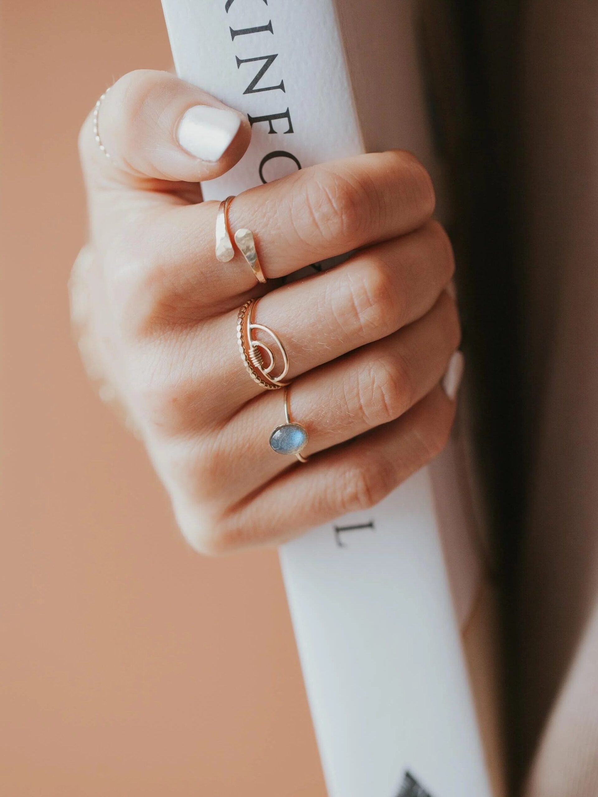 A person holding a book with their hand adorned with three elegant rings, including a gemstone ring.