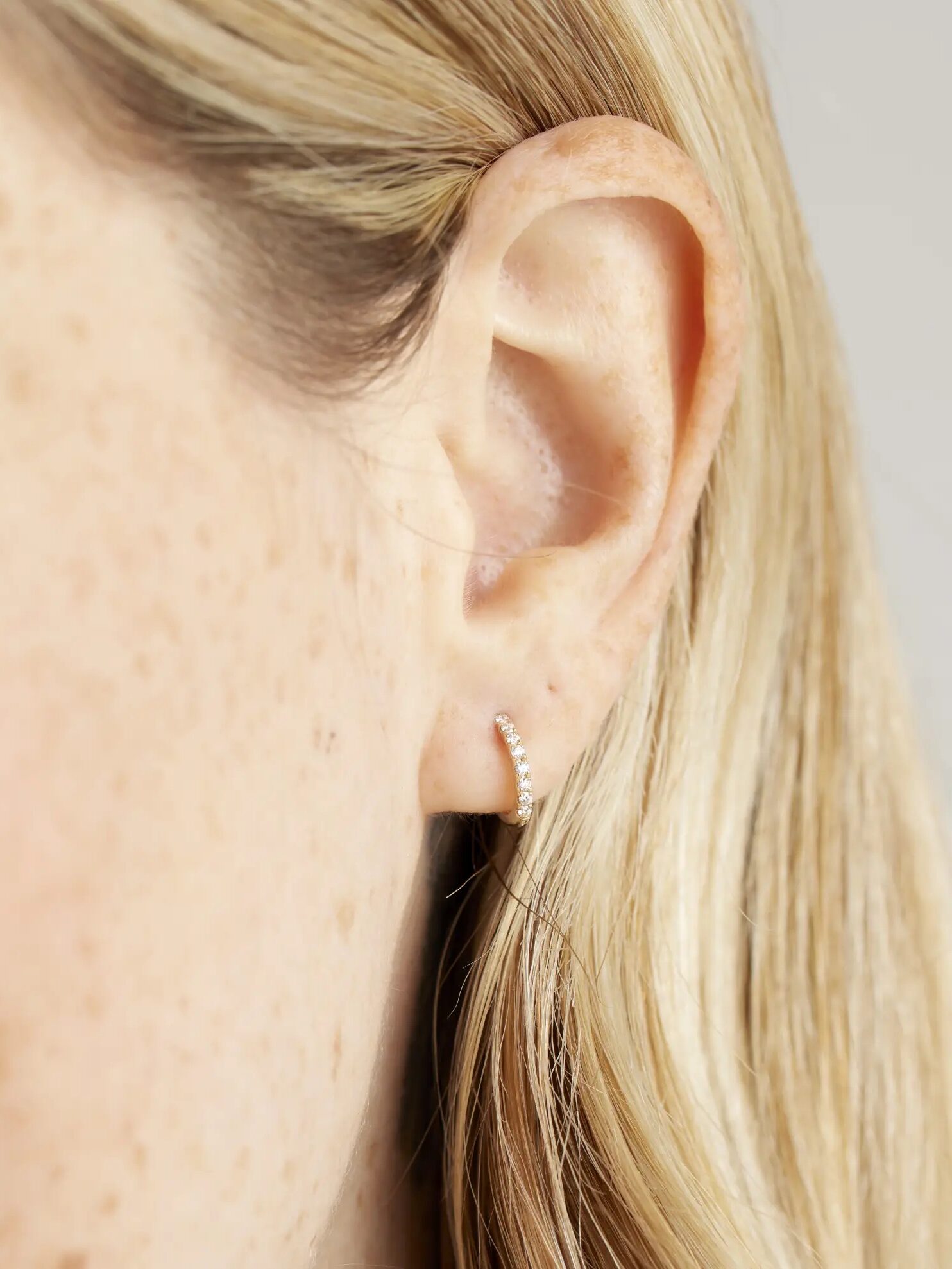 Close-up of a woman's ear showing a small diamond-studded earring, with a focus on her light freckled skin.