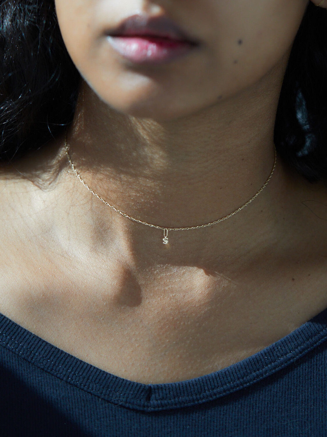 Close-up of a woman's lower face and neck, showing her wearing a gold necklace, with sunlight highlighting her skin.