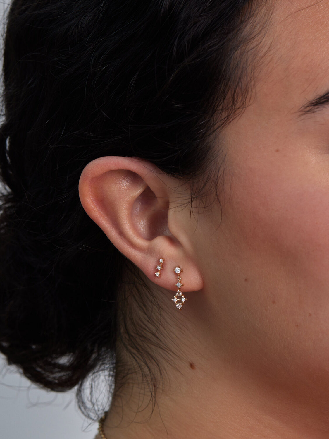 Close-up of a woman’s ear adorned with three delicate gold earrings, featuring small gems and star-shaped pendants.