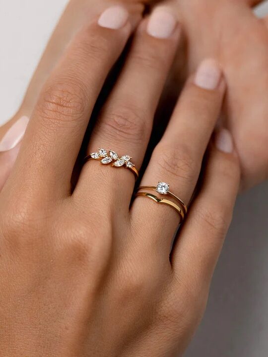 Close-up of a hand wearing three elegant rings, featuring a solitaire and two diamond-studded bands on different fingers.