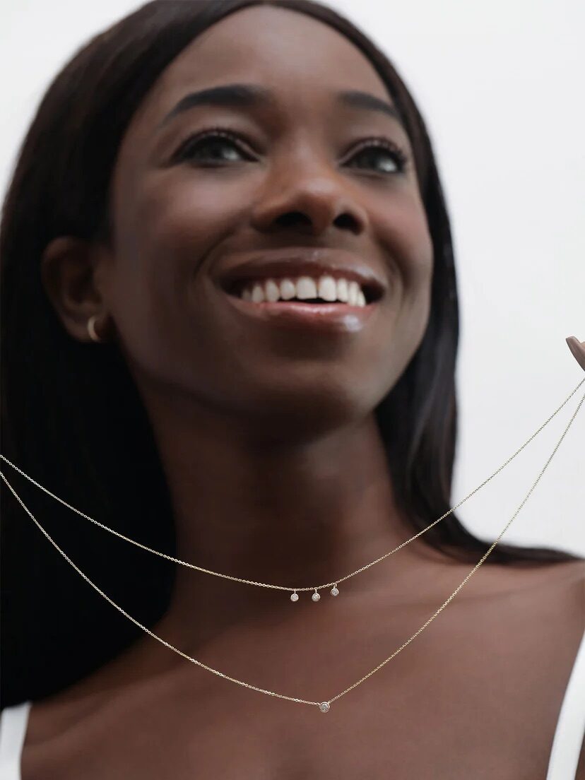 Close-up portrait of a smiling black woman wearing a white top and a delicate gold necklace.