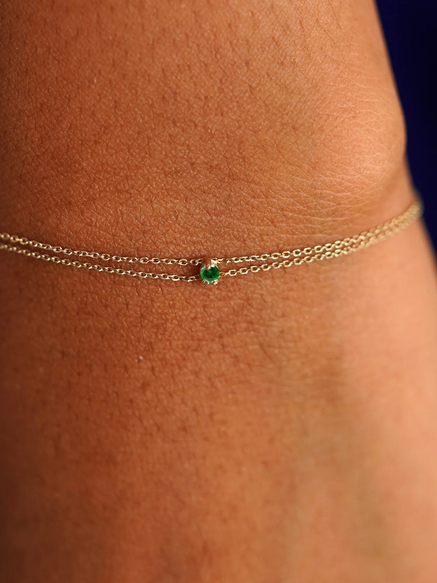 Gold bracelet with a green gemstone on a woman's wrist against a dark blue background.